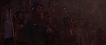 Movie still from “Escape from New York” (1981), directed by John Carpenter – A group of people in a room watching something on a screen; Medium shot, High angle