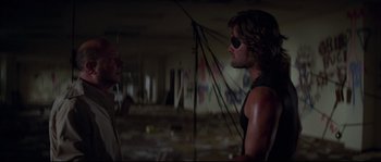 Movie still from “Escape from New York” (1981), directed by John Carpenter – Two men are standing next to each other in an abandoned building; Medium shot, Over the shoulder angle