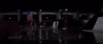 Movie still from “Escape from New York” (1981), directed by John Carpenter – A man standing in the middle of a parking lot at night; Extreme Wide shot, Low angle