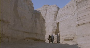 Movie still from “Essential Killing” (2010), directed by Jerzy Skolimowski – Two men are standing in the sand near a rock wall; Extreme Wide shot, Low angle