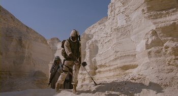 Movie still from “Essential Killing” (2010), directed by Jerzy Skolimowski – A soldier with a rifle in a rocky area; Wide shot, Low angle