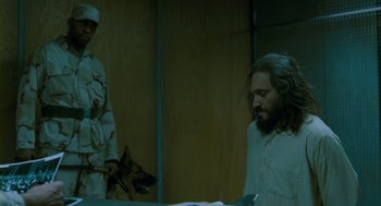 Movie still from “Essential Killing” (2010), directed by Jerzy Skolimowski – A man with long hair and a beard standing next to a man with a dog; Medium shot, Over the shoulder angle