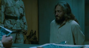 Movie still from “Essential Killing” (2010), directed by Jerzy Skolimowski – A man with a beard is sitting next to a dog; Medium shot, Over the shoulder angle