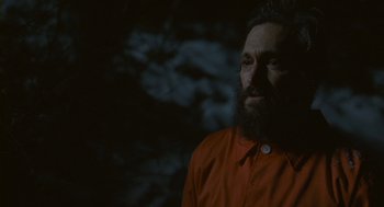 Movie still from “Essential Killing” (2010), directed by Jerzy Skolimowski – A man with a long beard wearing an orange shirt; Close Up shot, Low angle
