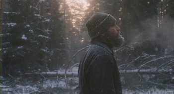 Movie still from “Essential Killing” (2010), directed by Jerzy Skolimowski – A man with a beard wearing a hat in the snow; Medium shot, Low angle