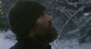 Movie still from “Essential Killing” (2010), directed by Jerzy Skolimowski – A man with a beard wearing a hat looking up; Close Up shot, Low angle