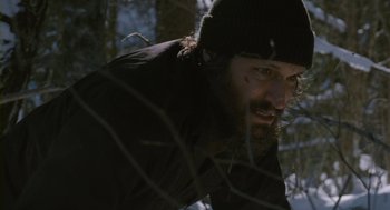 Movie still from “Essential Killing” (2010), directed by Jerzy Skolimowski – A man with a beard wearing a black hat; Close Up shot, Low angle
