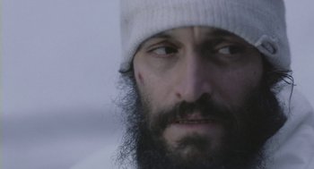 Movie still from “Essential Killing” (2010), directed by Jerzy Skolimowski – A man with a beard and a white hat; Close Up shot, Low angle