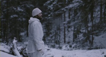 Movie still from “Essential Killing” (2010), directed by Jerzy Skolimowski – A man in a white coat standing in the snow; Medium shot, Low angle