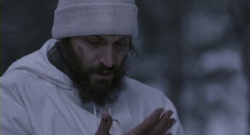 Movie still from “Essential Killing” (2010), directed by Jerzy Skolimowski – A man with a beard wearing a white hat and praying; Close Up shot, Low angle