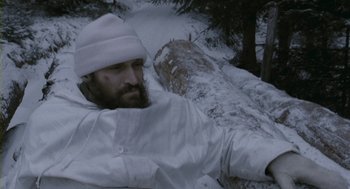 Movie still from “Essential Killing” (2010), directed by Jerzy Skolimowski – A bearded man in a white jacket and a white hat is standing in the snow; Medium shot, High angle