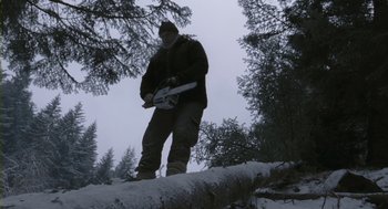 Movie still from “Essential Killing” (2010), directed by Jerzy Skolimowski – A man standing on top of a log holding a chainsaw; Wide shot, Low angle
