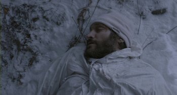 Movie still from “Essential Killing” (2010), directed by Jerzy Skolimowski – A bearded man laying on the ground in the snow; Close Up shot, Overhead angle