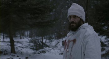 Movie still from “Essential Killing” (2010), directed by Jerzy Skolimowski – A man in a white jacket and a white hat in the snow; Medium shot, Low angle