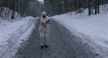 Movie still from “Essential Killing” (2010), directed by Jerzy Skolimowski – A man in a snow suit is standing on the side of a road; Wide shot, High angle