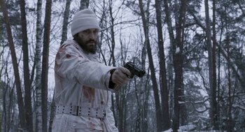 Movie still from “Essential Killing” (2010), directed by Jerzy Skolimowski – A man in a white jacket holding a gun in the woods; Medium shot, Low angle