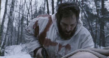 Movie still from “Essential Killing” (2010), directed by Jerzy Skolimowski – A man with a beard is holding a gun; Medium shot, Over the shoulder angle
