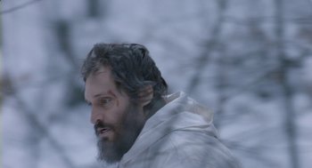 Movie still from “Essential Killing” (2010), directed by Jerzy Skolimowski – A man with a beard is walking in the snow; Close Up shot, Over the shoulder angle