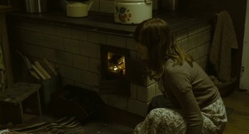Movie still from “Essential Killing” (2010), directed by Jerzy Skolimowski – A woman sitting in front of an open fire place; Medium shot, High angle