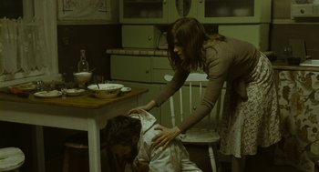 Movie still from “Essential Killing” (2010), directed by Jerzy Skolimowski – A woman helping a child lay on the floor in a kitchen; Medium shot, High angle