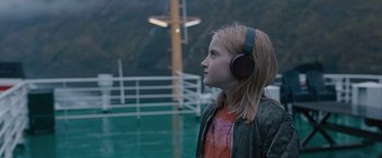 Movie still from “The Quake” (2018), directed by John Andreas Andersen – A young girl wearing headphones looking out over a body of water; Medium shot, High angle