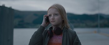Movie still from “The Quake” (2018), directed by John Andreas Andersen – A young girl wearing headphones talking on a cell phone; Close Up shot, Low angle