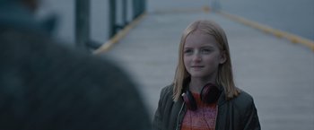 Movie still from “The Quake” (2018), directed by John Andreas Andersen – A young girl wearing headphones and standing on a sidewalk; Close Up shot, Over the shoulder angle