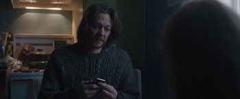 Movie still from “The Quake” (2018), directed by John Andreas Andersen – A man with long hair is looking at his cell phone; Medium shot, Over the shoulder angle