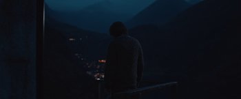 Movie still from “The Quake” (2018), directed by John Andreas Andersen – A man standing on a balcony at night looking out at the city lights; Wide shot, Over the shoulder angle