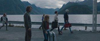 Movie still from “The Quake” (2018), directed by John Andreas Andersen – A group of people walking down a road near a body of water; Wide shot, Over the shoulder angle