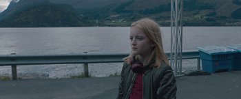 Movie still from “The Quake” (2018), directed by John Andreas Andersen – A young girl wearing headphones near a body of water; Medium shot, Over the shoulder angle