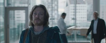 Movie still from “The Quake” (2018), directed by John Andreas Andersen – A man with long hair and a beard is standing in front of a window; Medium shot, Over the shoulder angle