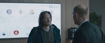 Movie still from “The Quake” (2018), directed by John Andreas Andersen – A man standing in front of a projector screen in a room; Medium shot, Over the shoulder angle
