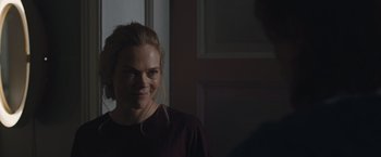 Movie still from “The Quake” (2018), directed by John Andreas Andersen – A woman smiling for the camera in front of a door; Close Up shot, Over the shoulder angle