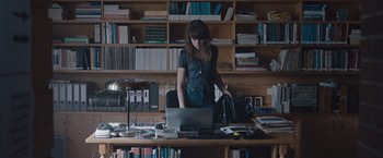 Movie still from “The Quake” (2018), directed by John Andreas Andersen – A woman standing in front of a laptop computer in a cluttered room; Medium shot, High angle
