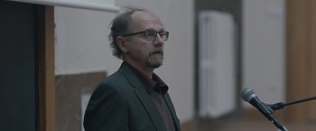 Movie still from “The Quake” (2018), directed by John Andreas Andersen – A man in a suit and glasses looking to his left; Close Up shot, Over the shoulder angle