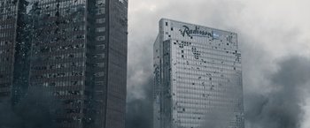 Movie still from “The Quake” (2018), directed by John Andreas Andersen – Smoke billows from a building on a cloudy day; Extreme Wide shot, Low angle