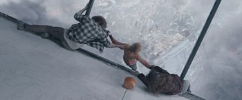 Movie still from “The Quake” (2018), directed by John Andreas Andersen – Two people are reaching for a ball on a skyscraper ledge; Wide shot, Overhead angle