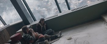 Movie still from “The Quake” (2018), directed by John Andreas Andersen – Two people sitting on the ground in front of a large window; Wide shot, High angle