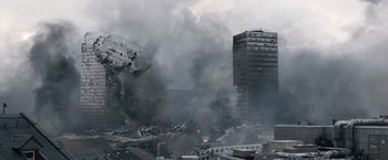 Movie still from “The Quake” (2018), directed by John Andreas Andersen – Smoke billows from a building that has been destroyed; Extreme Wide shot, High angle