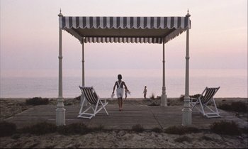 Movie still from “Eternity and a Day” (1998), directed by Theodoros Angelopoulos – A woman walking on a boardwalk near the ocean; Extreme Wide shot, High angle