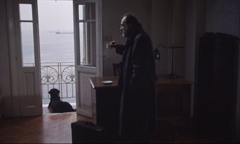 Movie still from “Eternity and a Day” (1998), directed by Theodoros Angelopoulos – A man standing in front of a window holding a cup of coffee; Wide shot, High angle