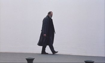 Movie still from “Eternity and a Day” (1998), directed by Theodoros Angelopoulos – An older man walking on a sidewalk near the water; Wide shot, Low angle