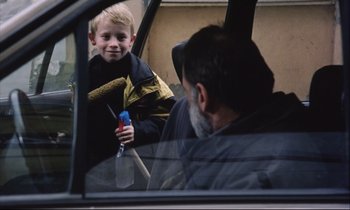 Movie still from “Eternity and a Day” (1998), directed by Theodoros Angelopoulos – A young boy holding a shovel in the back seat of a car; Medium shot, Over the shoulder angle