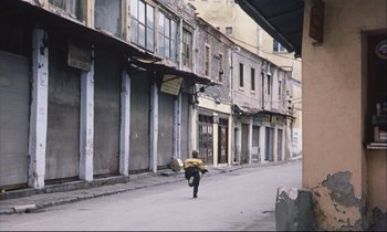 Movie still from “Eternity and a Day” (1998), directed by Theodoros Angelopoulos – A person walking down the street with a umbrella; Extreme Wide shot, High angle