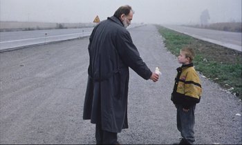 Movie still from “Eternity and a Day” (1998), directed by Theodoros Angelopoulos – A man and a boy holding a candle on the side of the road; Medium shot, Over the shoulder angle