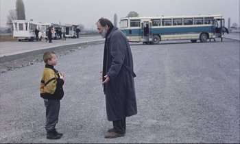 Movie still from “Eternity and a Day” (1998), directed by Theodoros Angelopoulos – A man and a boy standing in front of a bus on the street; Wide shot, Over the shoulder angle