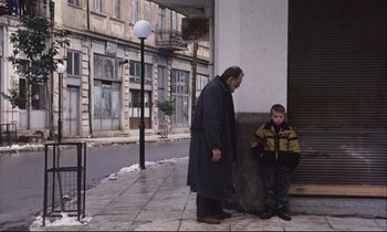 Movie still from “Eternity and a Day” (1998), directed by Theodoros Angelopoulos – A man and a boy standing next to each other on the sidewalk; Wide shot, Over the shoulder angle