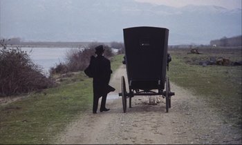 Movie still from “Eternity and a Day” (1998), directed by Theodoros Angelopoulos – A man standing next to an amish buggy on a dirt road; Extreme Wide shot, High angle