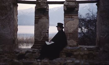 Movie still from “Eternity and a Day” (1998), directed by Theodoros Angelopoulos – A man sitting on a stone wall reading a book; Wide shot, Low angle